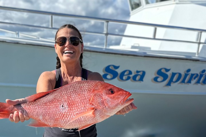 Person holding a large red fish in front of a boat named Sea Spirit.