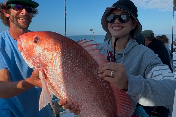 Person holding a large red fish on a boat, smiling, with another person beside.