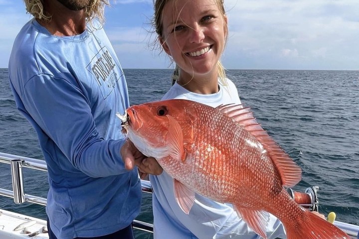 Two people on a boat holding a large red fish, smiling.