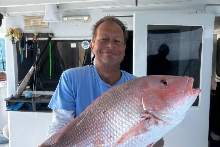 Person holding a large pink fish on a boat.
